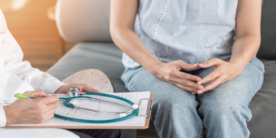 Patient sitting on a couch, across a doctor holding a chart