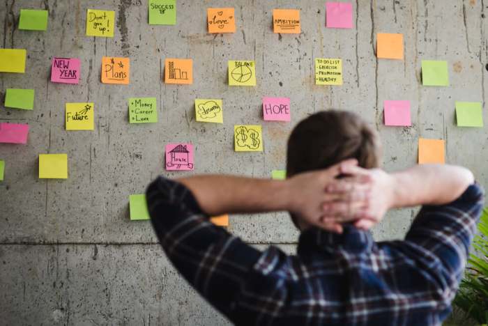 Back of entrepreneur sitting in office and look at colorful sticky message on cement wall. Work lifestyle concept. Selective focus.